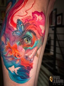 Colorful arm tattoo with swirling pink, red, orange, blue patterns and a blue butterfly near the upper arm, tattoo by Brian Ulibarri